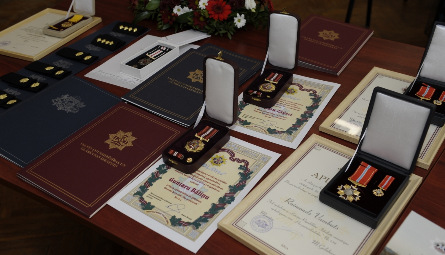 Uz galda stāv novietotas Pateicības, Apliecības, Diplomi, kā arī goda zīmes